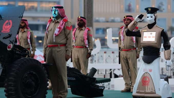 أول روبوت للشرطة التنفيذية في العالم يقف بجانب عناصر شرطة إماراتية يعدون مدفعًا عسكريًا لإطلاق النار للاحتفال بغروب الشمس ونهاية يوم الصيام للمسلمين الذين يحتفلون برمضان في وسط مدينة دبي في 31 أيار/مايو 2017 (AFP) الشرطة الإماراتية